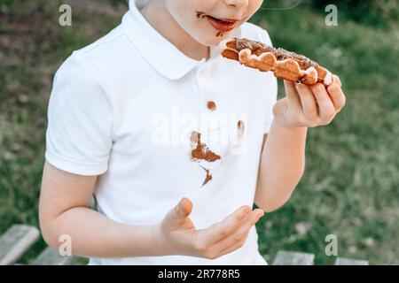 Taches de chocolat sur les vêtements blancs. Un garçon mangeant des gaufres belges avec des mains de chocolat collant. Vêtements gâtés. à l'extérieur Banque D'Images