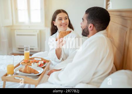 Femme offrant Croissant à mari pendant le petit déjeuner dans la chambre intérieure Banque D'Images