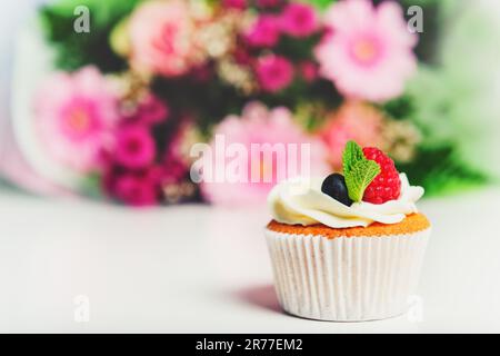 Un cupcake à la crème au beurre et aux baies fraîches, bouquet de fleurs roses sur fond Banque D'Images