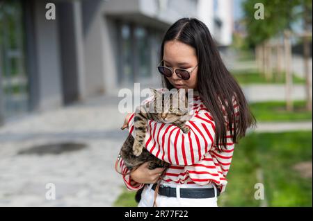 Jeune femme tenant le chat tabby dans ses bras à l'extérieur. Banque D'Images