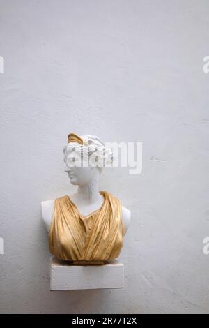 Buste antique de tête de femme contre le mur gris. Statue historique en robe dorée. Visage de femme antique sur fond clair. Photo de haute qualité Banque D'Images