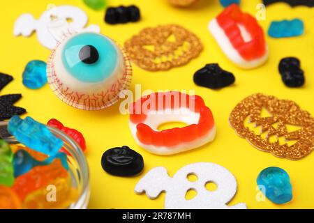 Savoureuses bonbons en gelée colorés et décorations d'Halloween sur fond jaune, gros plan Banque D'Images