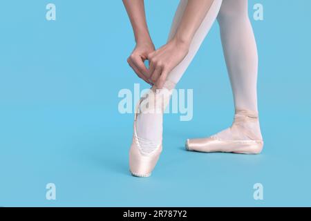 Jeune ballerine nouant des chaussures pointe sur fond bleu clair, gros plan Banque D'Images