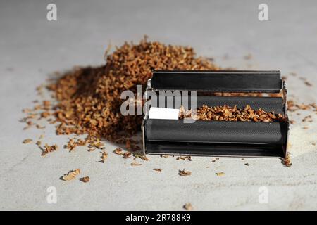 Rouleau avec filtre et tabac sur table gris clair. Fabrication de cigarettes roulées à la main Banque D'Images