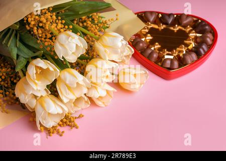 Bouquet de superbes tulipes, fleurs mimosa et boîte de bonbons au chocolat en forme de coeur sur fond rose Banque D'Images