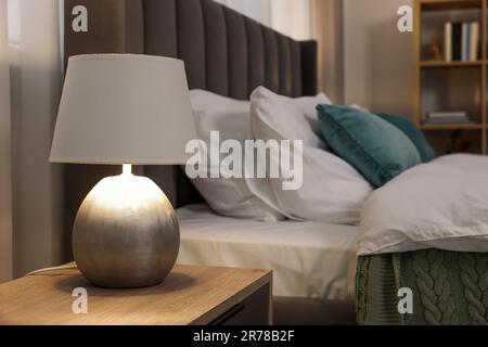 Lampe sur table de chevet en bois et lit gris confortable dans la chambre Banque D'Images