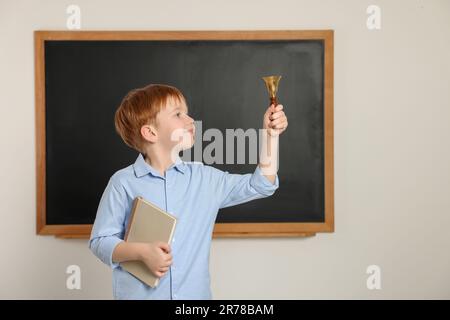 Petit garçon mignon sonnant la cloche de l'école dans la salle de classe Banque D'Images