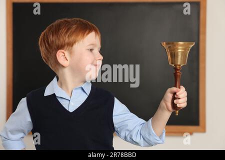 Petit garçon mignon sonnant la cloche de l'école dans la salle de classe Banque D'Images