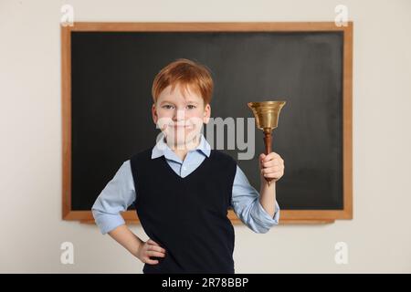 Petit garçon mignon sonnant la cloche de l'école dans la salle de classe Banque D'Images