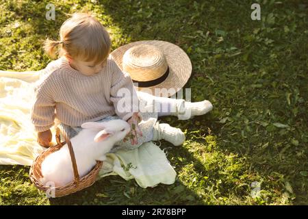 Petite fille mignonne nourrissant un adorable lapin sur l'herbe verte à l'extérieur, au-dessus de la vue et de l'espace pour le texte Banque D'Images