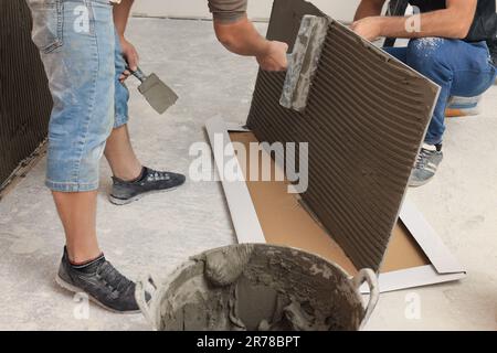 L'employé répandant le mélange d'adhésif sur les carreaux avec une spatule, gros plan Banque D'Images