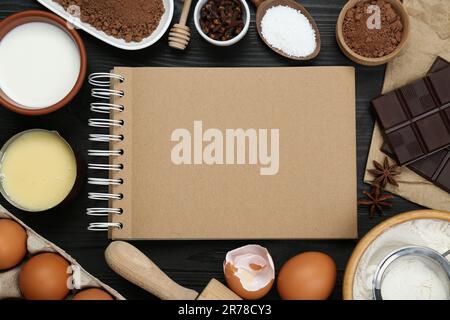 Livre de recettes vierge entouré de différents ingrédients sur table en bois noir, plat. Espace pour le texte Banque D'Images