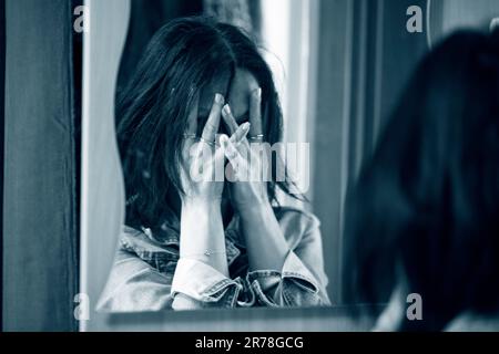 Une femme cachant son visage avec ses mains. Reflété dans un miroir, photographie monochrome. Banque D'Images