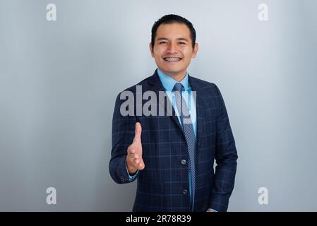 Un jeune homme d'affaires, une ethnie hispanique sourit entre accolades, fait des vagues avec sa main ouverte devant lui, porte un costume d'affaires, une personne Banque D'Images