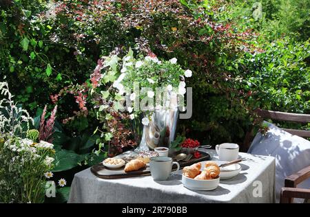 Petit déjeuner continental sur la table du jardin. Style de vie de pays ou concept de matin de week-end. Paysage rural paisible. Banque D'Images