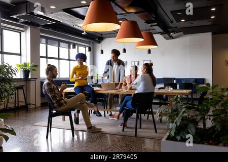 Heureux collègues masculins et féminins utilisant un ordinateur portable parlant dans une réunion de bureau occasionnelle Banque D'Images