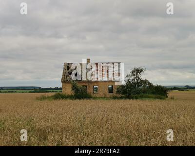 Ancienne ferme en briques dans la campagne avec nuages de tempête dans le ciel. Il y a un petit pré d'herbe et un vieux pommier autour de la maison. Banque D'Images