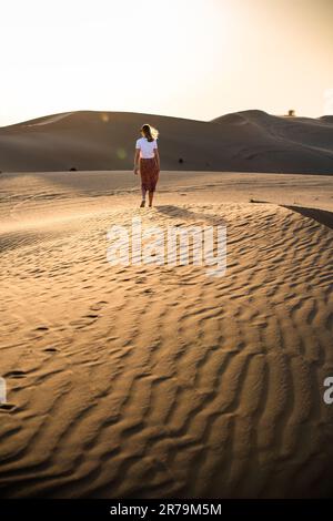 Une femme seule marchant dans un désert au lever du soleil, éclairée par la lumière chaude du matin Banque D'Images