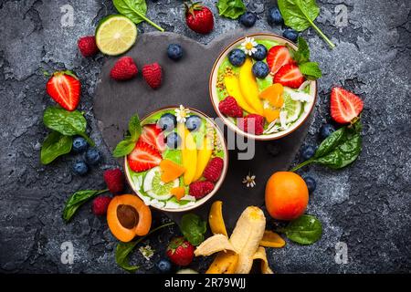 Smoothie vert dans des bols pour un petit déjeuner sain. Smoothie frais bio à base d'épinards, de banane, de spiruline, de wheatgrass et de lime avec baies et fruits Banque D'Images