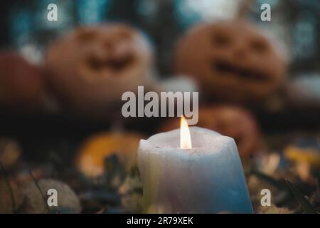 Bougie brûlante gros plan sur les têtes de citrouilles d'Halloween floues arrière-plan. Citrouille avec visage souriant sculpté à l'extérieur. Jack-O-Lantern extérieur. Hallo Banque D'Images