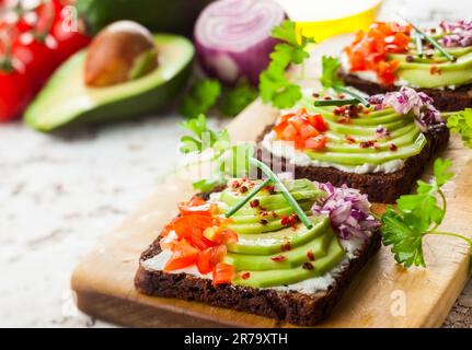 Sandwichs ouverts végétariens frais sur du pain noir avec avocat, tomate et oignon rouge sur le panneau de bois. Concept alimentation saine. Mise au point sélective Banque D'Images