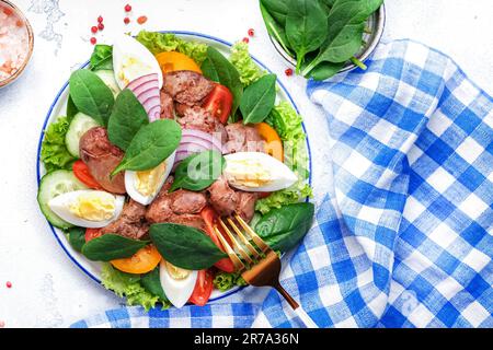 Salade Périgord avec foie de poulet rôti, tomates rouges, concombres, œufs durs, laitue et épinards. Arrière-plan de la table de cuisine noire, vue du dessus Banque D'Images