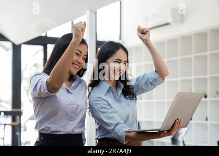 Deux jeunes femmes d'affaires manifestent une joyeuse expression de succès au travail en souriant avec un ordinateur portable dans un bureau moderne Banque D'Images