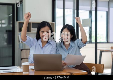 Deux jeunes femmes d'affaires manifestent une joyeuse expression de succès au travail en souriant avec un ordinateur portable dans un bureau moderne Banque D'Images