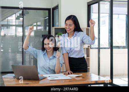 Deux jeunes femmes d'affaires manifestent une joyeuse expression de succès au travail en souriant avec un ordinateur portable dans un bureau moderne Banque D'Images