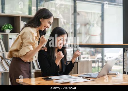 Deux jeunes femmes d'affaires manifestent une joyeuse expression de succès au travail en souriant avec un ordinateur portable dans un bureau moderne Banque D'Images