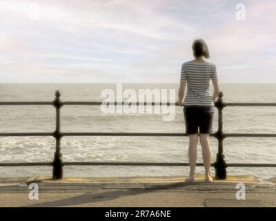 Vue arrière d'une femme adulte du Caucase portant un short et un t-shirt debout sur le front de mer de North Bay de Scarborough, avec vue sur la mer. Banque D'Images