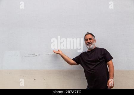 Homme adulte avec barbe et ventre, t-shirt noir pointant vers l'espace de copie Banque D'Images