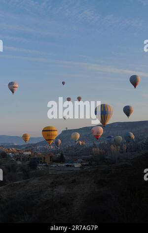 Un groupe de ballons à air chaud aux couleurs vives s'envolent dans le ciel au-dessus d'un paysage pittoresque avec des collines et de la verdure Banque D'Images