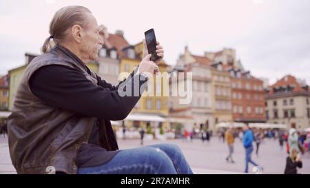 Senior s'assoit sur les marches et capture des sites à l'aide d'un smartphone dans le centre historique d'une vieille ville européenne. Place du Palais, vieille ville de Varsovie Banque D'Images