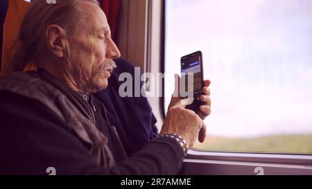 Homme âgé voyageant en train et prenant des photos du paysage par la fenêtre à l'aide d'un smartphone Banque D'Images