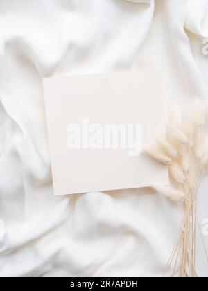 Maquette de feuille de papier blanc vierge, enveloppe et branche florale sèche sur fond textile blanc neutre. Modèle d'invitation de mariage esthétique minimaliste Banque D'Images