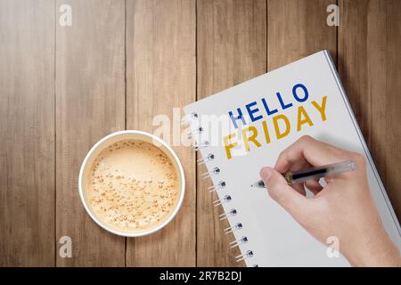 Tasse à café avec main humaine écrire Bonjour vendredi texte sur un bloc-notes. Concept « Vendredi heureux » Banque D'Images