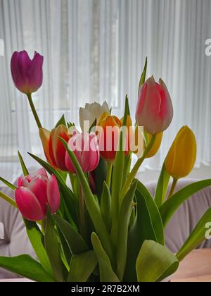 Un vase au sommet d'une table en bois remplie de tulipes colorées Banque D'Images