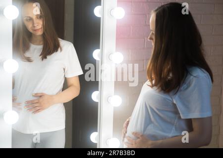 Femme enceinte avec un gros ventre devant le miroir, debout dans la pièce Banque D'Images
