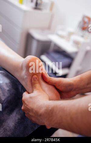 Gros plan du pied féminin avec un massage doux. La masseuse tient la jambe de la femme dans ses mains. Le jeune client se trouve et aime la procédure de détente dans le salon de beauté Banque D'Images