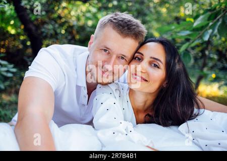 Portrait d'un jeune couple souriant amoureux sur fond de jardin ou de nature. Belle femme brune aux cheveux affectueusement hale homme attrayant. Heureux Banque D'Images
