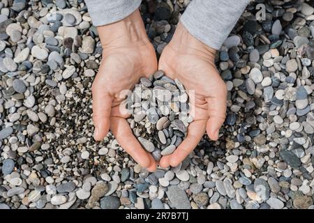 Les mains des femmes avec des cailloux de mer. Plage de galets de mer gros plan, galets ronds sombres et galets secs gris, idée de photo de haute qualité pour l'écran Banque D'Images