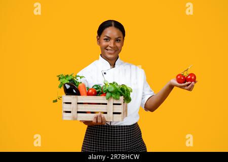 Femme de chef souriante noire tenant une caisse en bois avec des légumes biologiques Banque D'Images