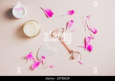 Rouleau de quartz rose, gua sha et crèmes pour le visage sur fond rose, soins du visage et du cou, soins spa. Banque D'Images