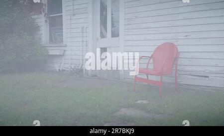 Chaise en métal rouge vif vintage contre un ancien hangar de ferme blanc en bois Banque D'Images