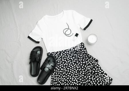 T-shirt blanc, jupe noire, sandales et accessoires sur fond gris. Vue sur la tenue de jour décontractée pour femme. Look estival tendance et stylé. Mél Banque D'Images