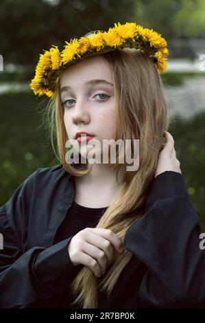 Une fille sérieuse et mystérieuse dans une couronne de pissenlits. Une fille aux cheveux longs et épais est triste au printemps dans la rue. Banque D'Images