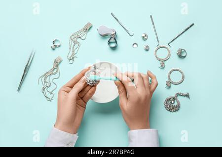 Femme qui nettoie de magnifiques boucles d'oreilles avec une brosse à dents sur fond de couleur Banque D'Images