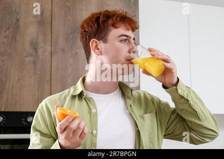 Un jeune homme boit du jus d'orange dans la cuisine Banque D'Images