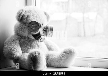 Un ours en peluche est assis sur la fenêtre d'une maison dans un masque à gaz, armes chimiques, guerre, blanc noir Banque D'Images